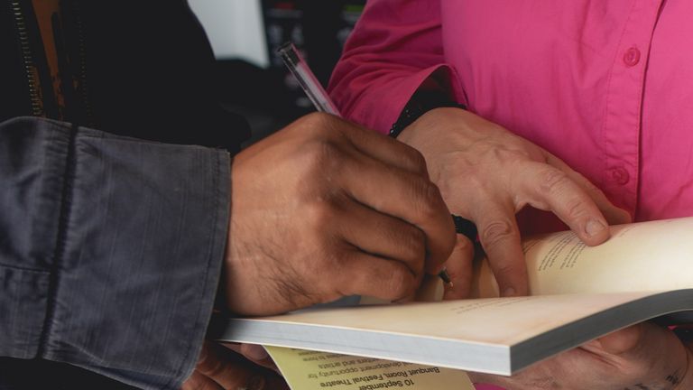 Close-up of hands signing an open book at Our Worlds event during a book signing.